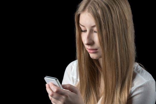 Attractive young girl feels depressed after reading bad news on her mobile cellular phone. Isolated on black.