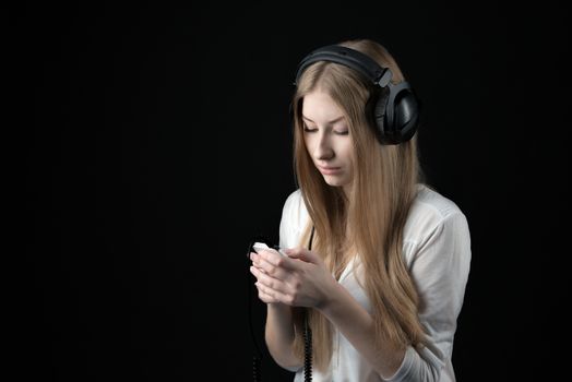 Close up portrait of a serious teenager girl in wired headphones listening music from personal phone