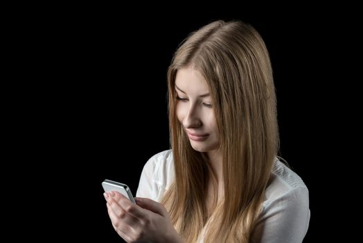 Young pretty girl enjoying social network on her personal cellular mobile phone. Isolated on black.