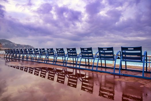 Blue chairs along the Promenade des Anglais on the Mediterranean Sea at Nice, France along the French Riviera.