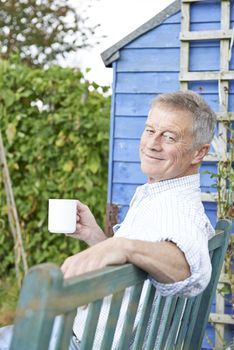 Senior Man Relaxing In Garden With Cup Of Coffee