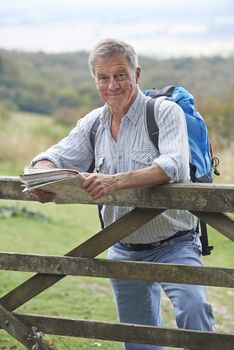 Senior Man Hiking In Countryside Resting By Gate