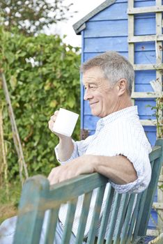 Senior Man Relaxing In Garden With Cup Of Coffee