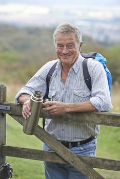 Portrait Of Senior Man On Hike In Countryside Resting By Gate And Having Hot Drink