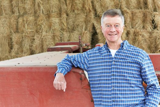 Farmer Standing Next To Farm Machinery In Barn