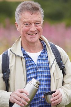 Senior Man Pouring Hot Drink From Flask On Walk