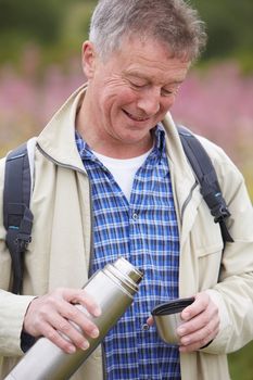 Senior Man Pouring Hot Drink From Flask On Walk