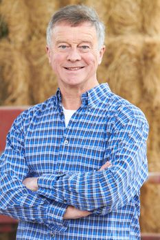 Farmer Standing In Front Of Bales And Old Farm Equipment