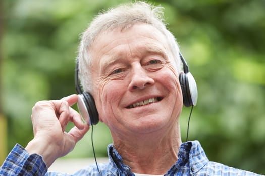 Senior Man Relaxing Listening To Music On Headphones In Garden
