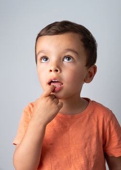 Cute three year old boy portrait, toddler puts one finger in his mouth.