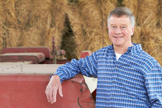 Farmer Standing In Front Of Bales And Old Farm Equipment