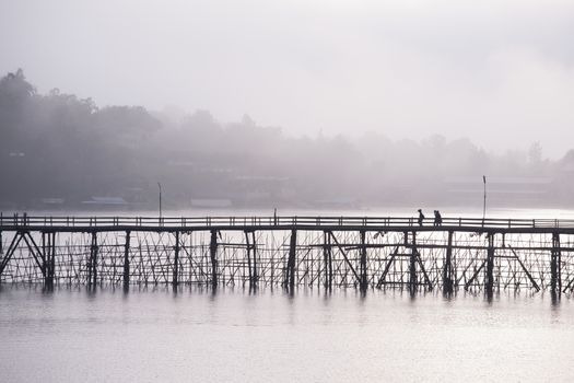 Wooden bridge across through river with foggy background at sunrise reflection on water located Kanchanaburee province west of Thailand