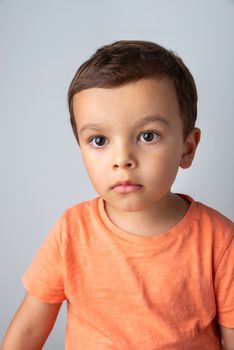 Cute three year old boy portrait, toddler wearing orange tee shirt and shot against a light grey background.