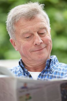 Senior Man Reading Newspaper Outdoors At Home