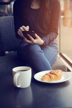 Asian female typing text message with coffe and Croissant