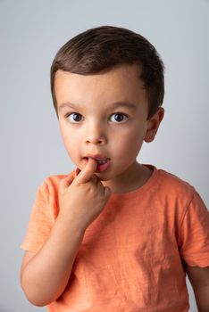 Cute three year old boy portrait, toddler puts one finger in his mouth.