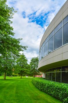 Green hedge and mowed lawn along round shaped wall of the office building