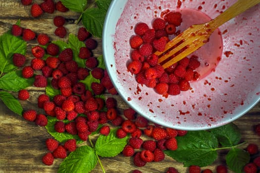 Ripe sweet raspberries in bowl, wooden fork on wooden table. Close up, top view. Red fresh raspberries on brown rustic wood background. flat lay with copy space.