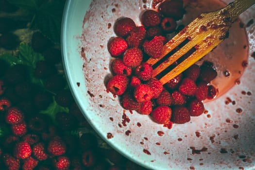 Ripe sweet raspberries in bowl, wooden fork on wooden table. Close up, top view. Red fresh raspberries on brown rustic wood background. flat lay with copy space.