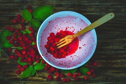 Ripe sweet raspberries in bowl, wooden fork on wooden table. Close up, top view. Red fresh raspberries on brown rustic wood background. flat lay with copy space.