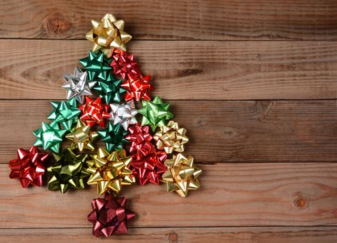 Overhead view of a group of assorted bows arranged into a Christmas Tree shape. The bows are on a rustic wood floor. Vertical format.