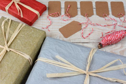 Overhead shot of a group of blank gift tags surrounded by wrapped Christmas presents on a white rustic table. Horizontal format with focus on the gift tags.