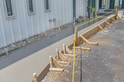 Horizontal shot of a freshly poured concrete sidewalk with caution tape in front of it.