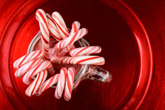 High angle shot of a group of Christmas candy canes in a mason jar on a red plate.