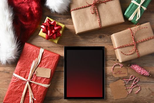 Christmas Presents Tablet Computer and wrapping materials on a rustic wood table.