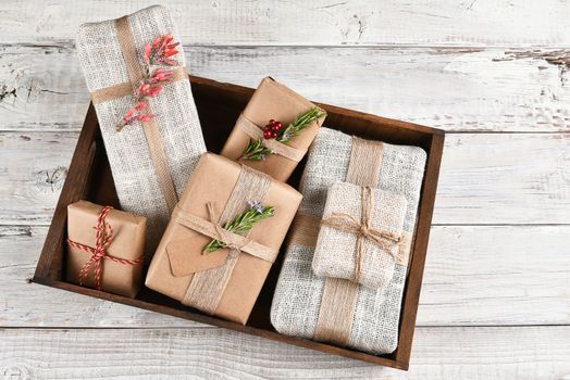 Paper and fabric wrapped Christmas presents in a wood box on a rustic whitewashed wood table.