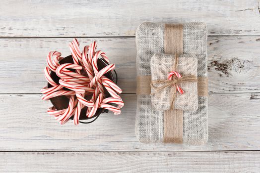 Top view of a bucket filled with holiday candy canes and a burlap fabric wrapped Christmas present. 