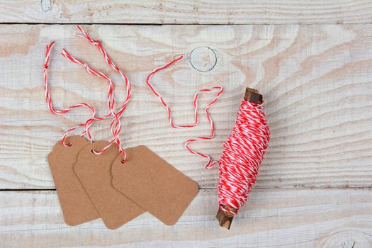 High angle view of blank Christmas Gift tags next to a spool of string on a whitewashed rustic wood table. The tags are blank and the string is wound around a twig.