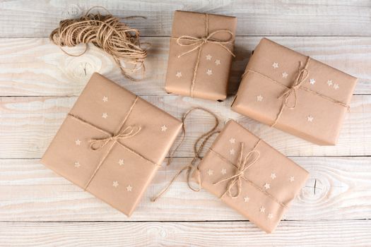 High angle image of four brown packages wrapped with plain brown paper on a white rustic wood table. Paper stars on the boxes that are tied with twine.  
