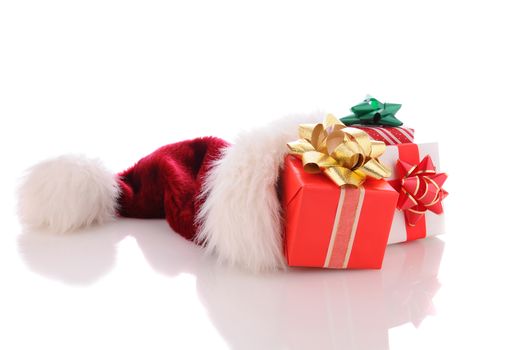 Wrapped Christmas presents spilling out of a Santa hat on a white background with reflection.