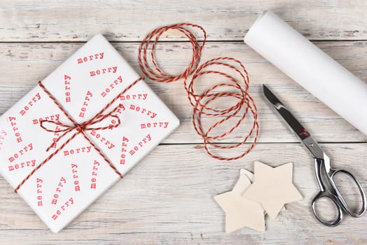 Christmas present stamped with the word Merry. High angle shot with scissors, twine and roll of wrapping paper. 