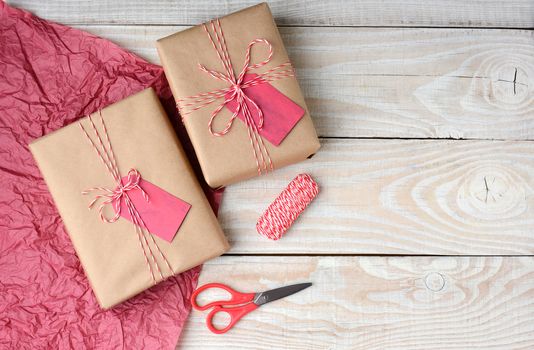 Overhead view of two Christmas presents wrapped in plain brown paper and tied with red and white string, Scissors,, spool of string and red tissue paper with copy space.