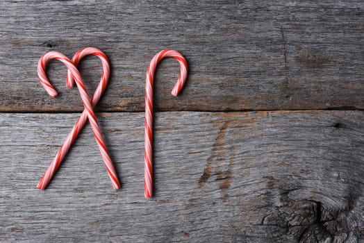 High angle shot of three holiday candy canes on a rustic wood table. Two pieces overlap. Horizontal format with copy space.