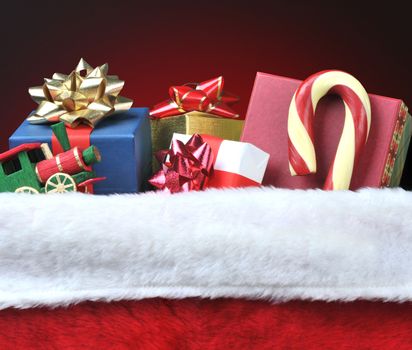 Closeup of a Christmas Stocking filled with toys, presents and a candy cane. Square format on a light to dark red background.