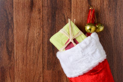 Closeup of a Christmas stocking filled with presents hanging from a hook on a wood wall. Two jingle bells hang from the hook also in vertical format.