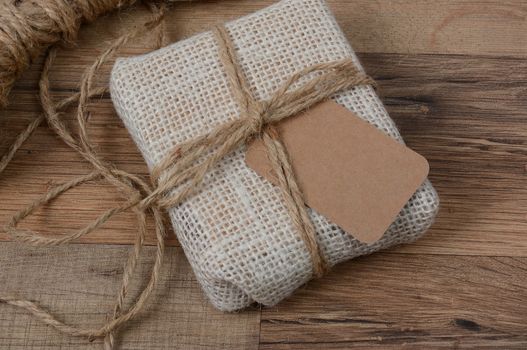 Closeup of a small fabric present with a blank gift tag on a wood table. 