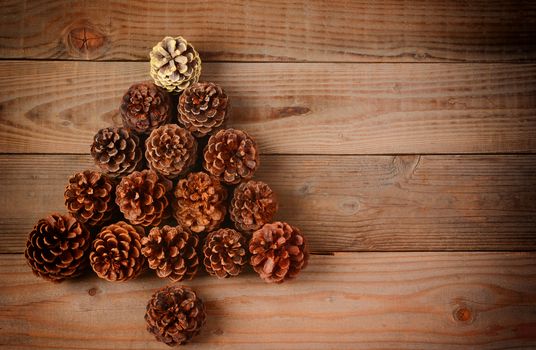 A group of pine cones arranged in a Christmas Tree shape on a rustic wood floor, Horizontal format with an instagram retro look and copy space.