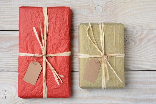 High angle shot of two presents on a white wood rustic table. Wrapped in crumpled tissue paper with blank gift tags. Horizontal format.