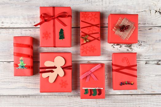 High angle view of a variety of red wrapped Christmas presents on a rustic white wood surface.
