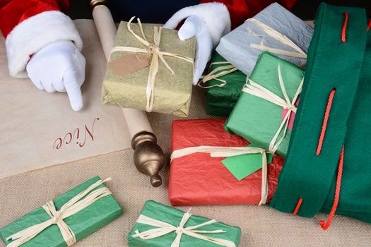 Santa Claus checking his list as he packs his bag for delivery on Christmas Eve. Horizontal format closeup showing only Santa's hands, presents and his bag.