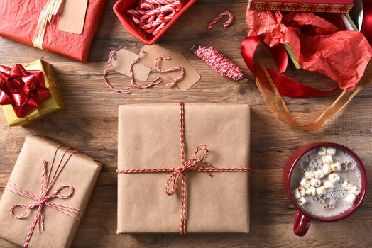 High angle view of Christmas presents and hot chocolate on a wood table. Plain wrapped gifts with string, candy canes and ribbon.