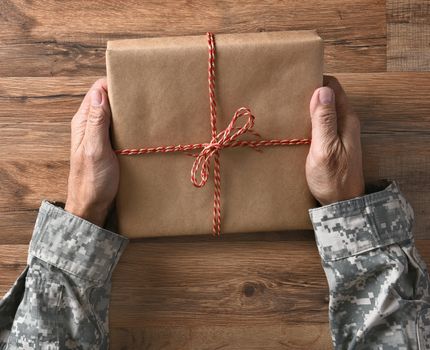 Closeup of a soldiers hands holding a plain wrapped parcel, over a wood background.