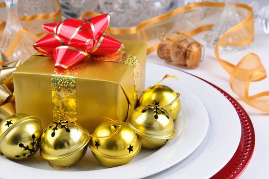 Closeup of a decorated holiday table with presents, bells, ribbons, plates and champagne glasses. Horizontal format.