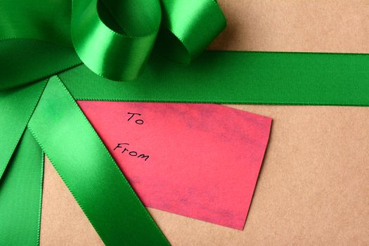 Closeup of a gift tag on a Christmas present. The package is wrapped in plain brown paper and Green Ribbon. The red tag has the words To and From printed on it. Horizontal format.