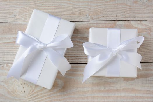 High angle image of two presents wrapped in white paper and ribbons. Horizontal format on a whitewashed rustic wood table.
