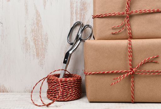 Closeup of two plain brown paper wrapped Christmas presents with scissors and twine.